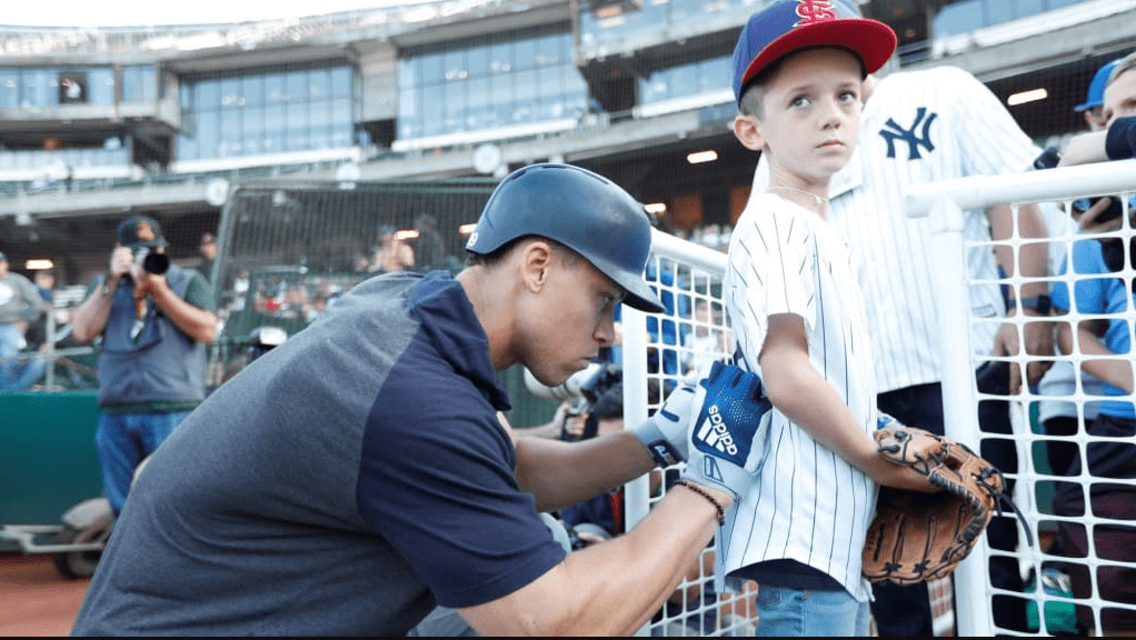 Aaron Judge is signing an autograph for a young Yankees fan at Steinbrenner Field.