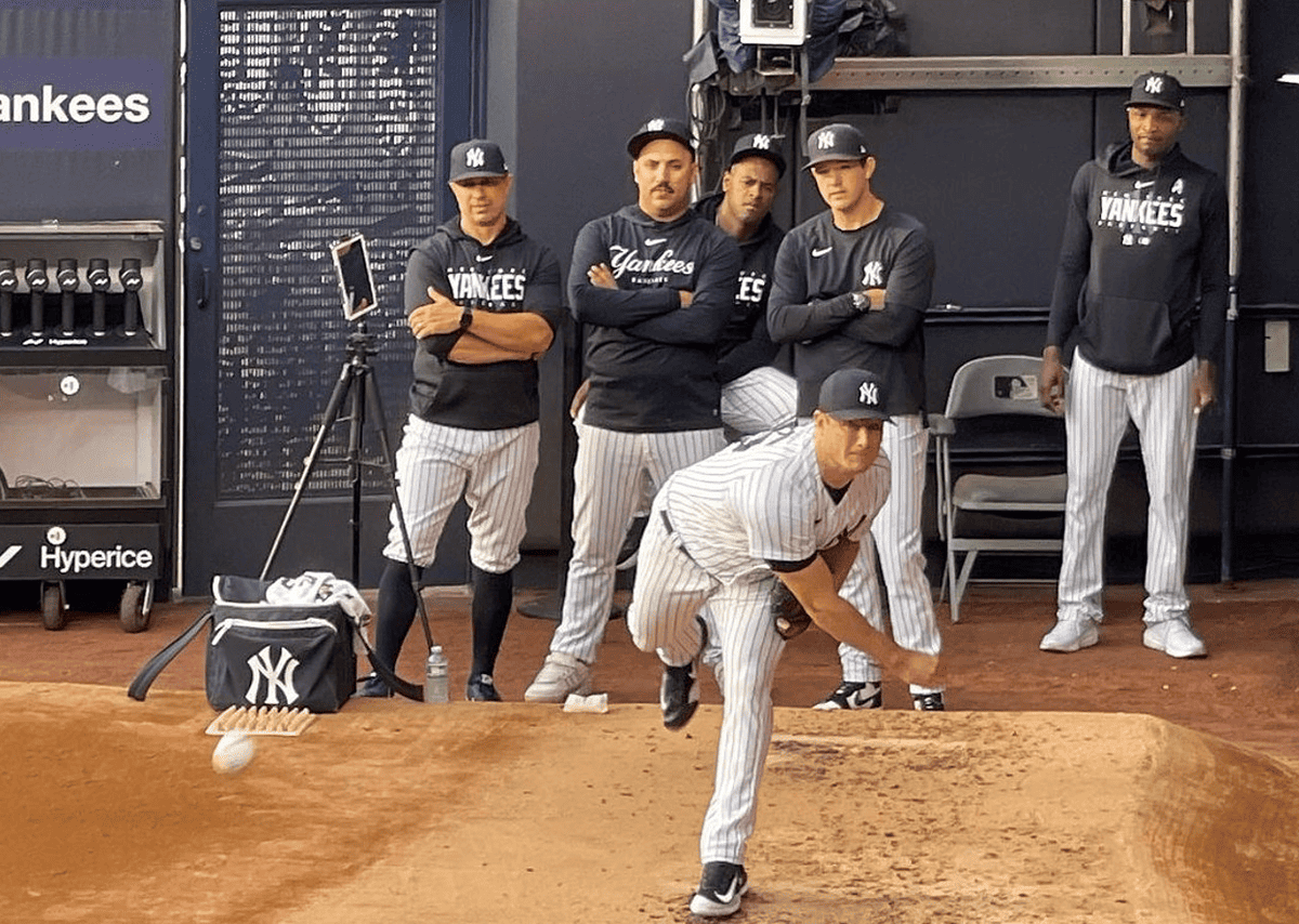 Gerrit Cole pitches as other Yankees starters look at him.