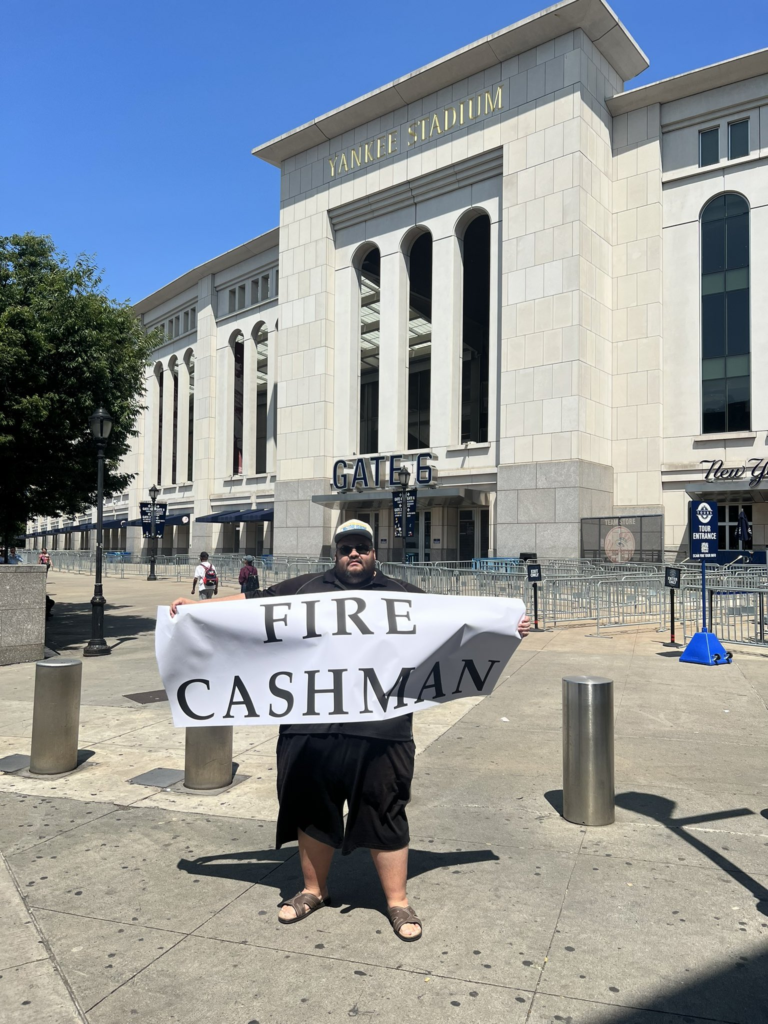 Yankees fan Jon stands holding "FIRE CASHMAN" sign on August 1, 2023, outside Yankee Stadium.