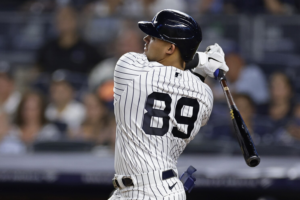 Jasson Dominguez in his New York Yankees uniform, standing confidently on the baseball field, representing the team's top prospect according to Major League Baseball rankings.