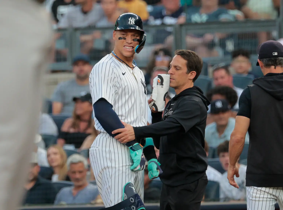 18 de junio de 2024. Aaron Judge, jardinero de los Yankees de Nueva York, hace una mueca mientras es atendido por el entrenador del equipo debido a una lesión en la mano en el Yankee Stadium.
Aaron Judge es examinado por el entrenador de los Yankees tras recibir un golpe en la mano.