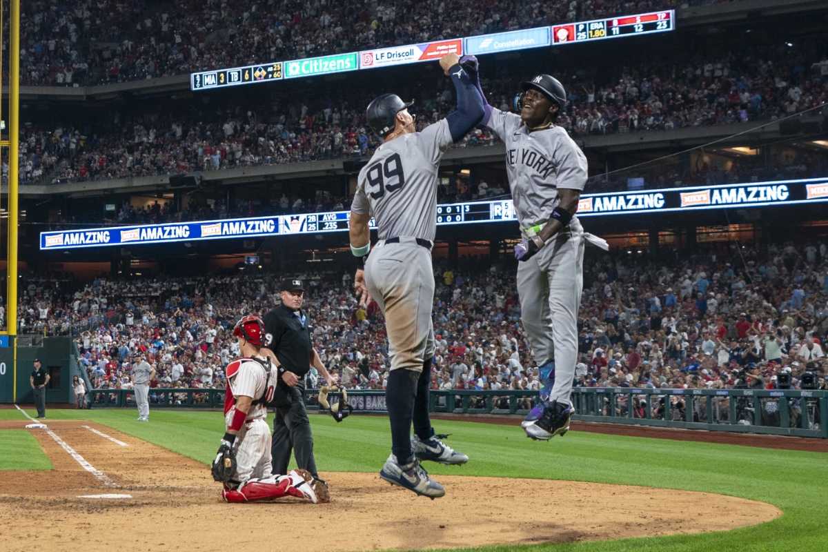 Jazz Chisholm Jr. de los Yankees de Nueva York, a la derecha, celebra su jonrón de tres carreras con Aaron Judge, en el centro, mientras el receptor de los Filis de Filadelfia J.T. Realmuto, a la izquierda, observa durante la séptima entrada de un partido de béisbol, el martes 30 de julio de 2024, en Filadelfia.