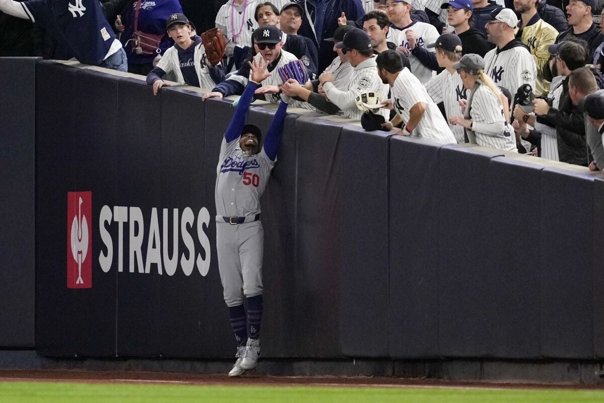 Los aficionados interfieren con una bola de foul atrapada por el jardinero derecho de los Dodgers de Los Ángeles, Mookie Betts, durante la primera entrada del cuarto partido de las Series Mundiales de béisbol contra los Yankees de Nueva York, el martes 29 de octubre de 2024, en Nueva York.  