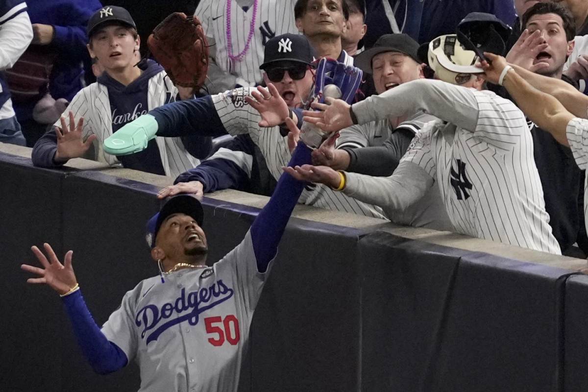 Fans interfere with a foul ball caught by LA Dodgers right fielder Mookie Betts during the first inning in Game 4 of the baseball World Series against the New York Yankees, Tuesday, Oct. 29, 2024, in New York.