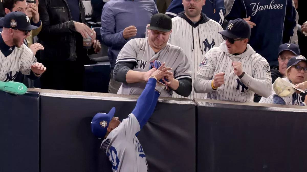 Fans interfere with a foul ball caught by LA Dodgers right fielder Mookie Betts during the first inning in Game 4 of the baseball World Series against the New York Yankees, Tuesday, Oct. 29, 2024, in New York.