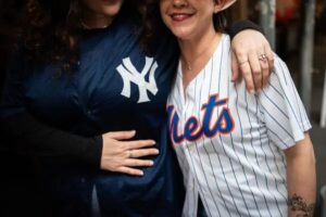 A Mets fan on the right hugs a Yankees fan on the left, capturing a moment of unity between rival teams.