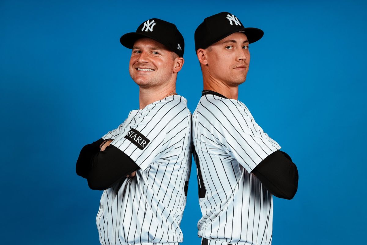 larke Schmidt and Luke Weaver, both in Yankees pinstripes and black caps, stand back-to-back with arms crossed against a blue backdrop during the Yankees’ media day on February 18, 2024.