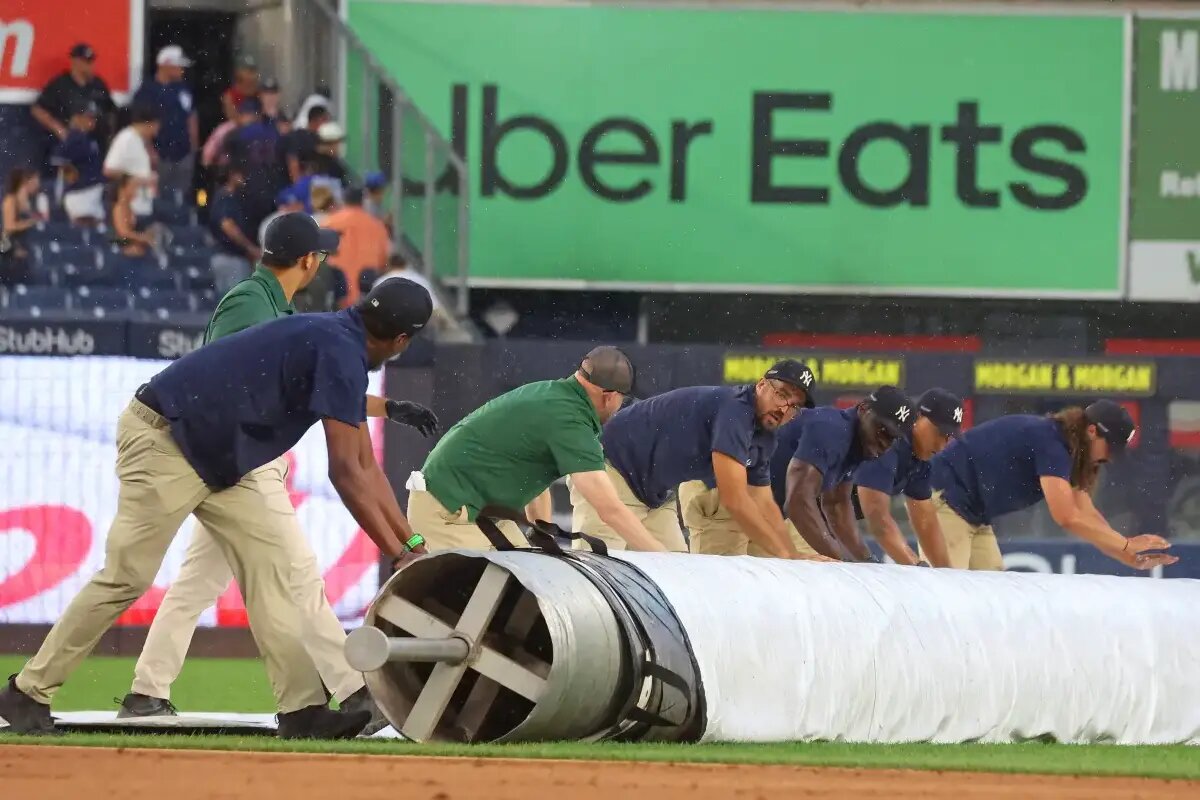 El equipo de tierra enrolla la lona en el campo del estadio de los Yankees.
